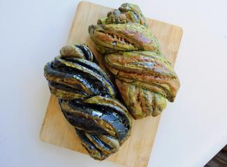 an overhead shot of two loaves of braided challah bread with black and green swirls.