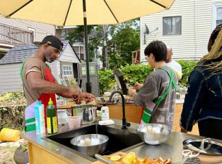 Two men cook in an outside kitchen